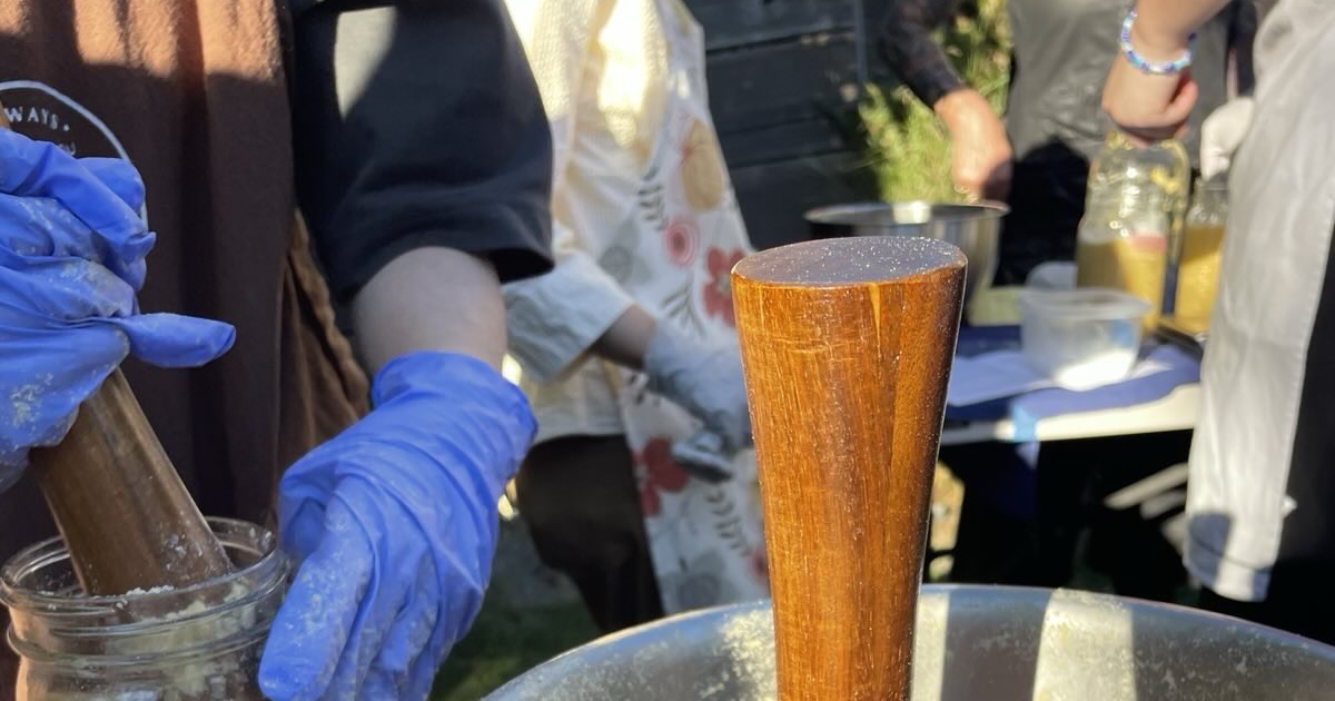Hands in nitrile gloves packing fresh miso into a jar with a wooden tamper.